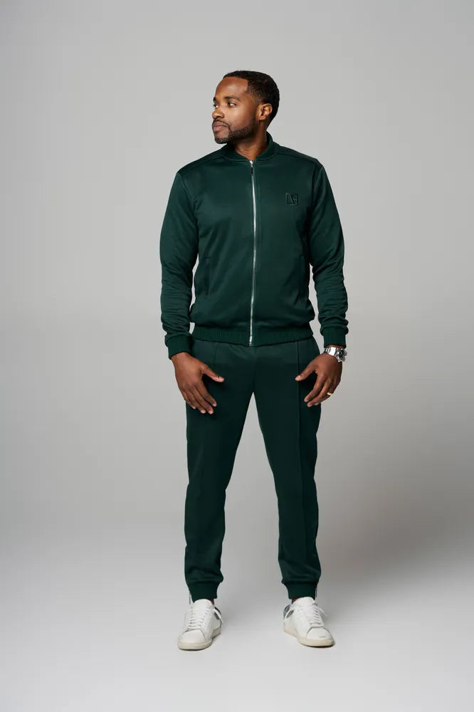 a man is standing wearing forest green tracksuit