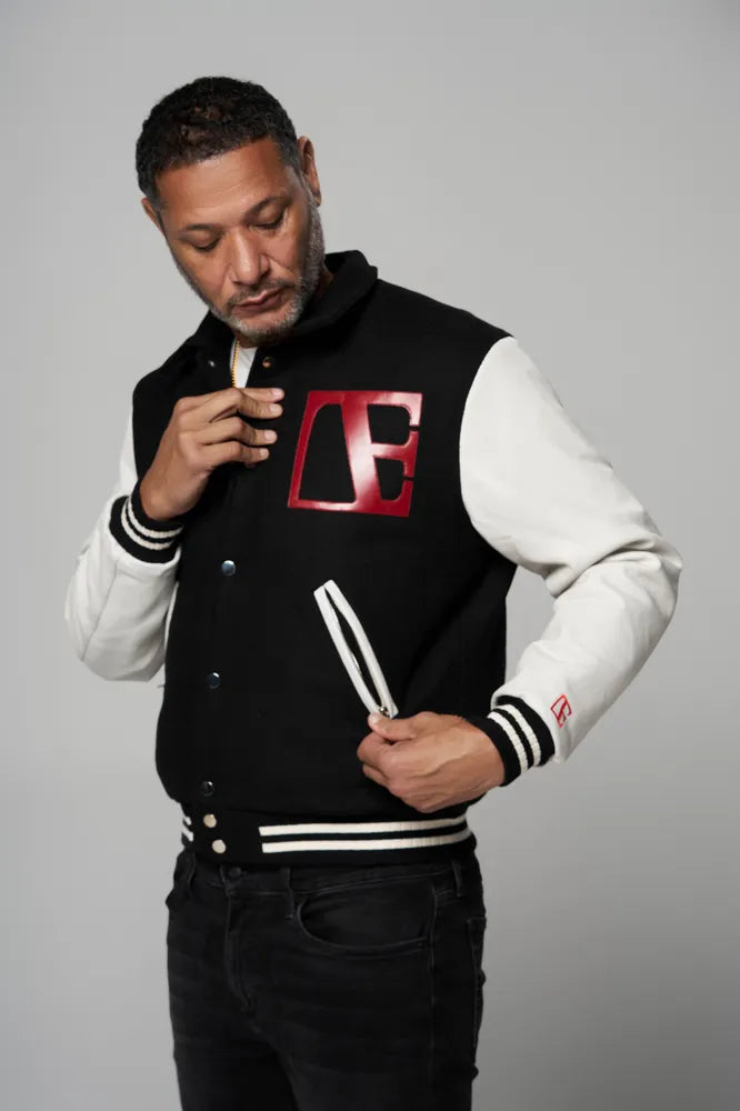 a man is wearing black letterman jacket looking at the red logo